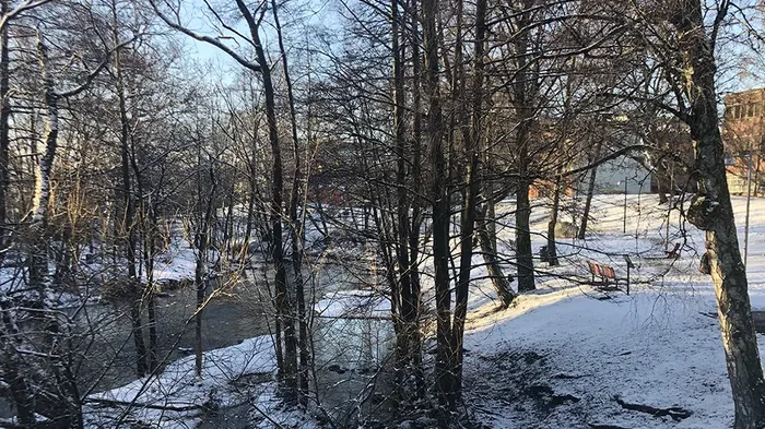 en elv med trær rundt, snø på bakken, murbygninger i bakgrunnen
