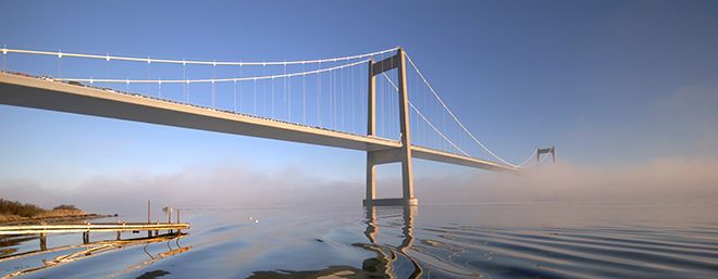 En bro som strekker seg inn i tåkelagt sjø. Blå himmel. 