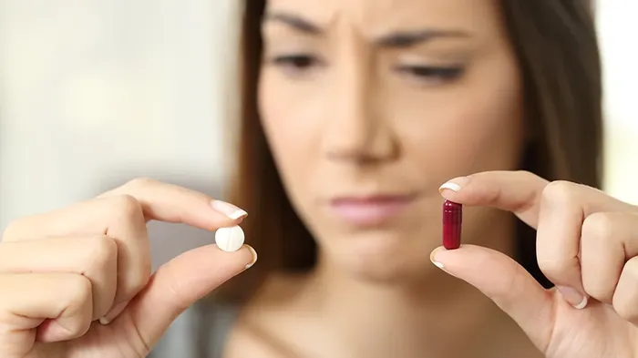 Woman looking at a red and a white pill, looking indecisive