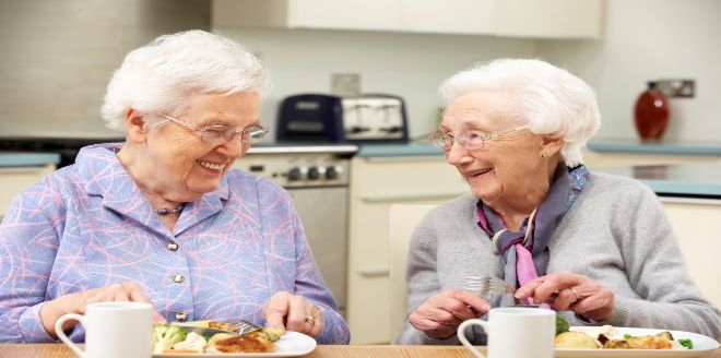 Two elderly women eating together in a kitchen