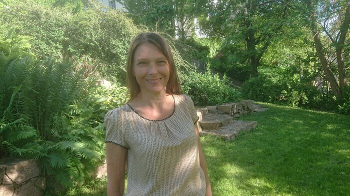 Bildet viser en kvinne med brunt, halvlangt hår som står i en hage.