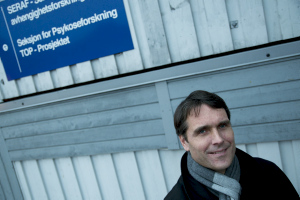Professor Ole A. Andreassen foran grå vegg med blått skilt med hvit tekst.