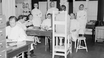 Leger med en pasient på Hudavdelingen, 1951. Stolen pasienten sitter på finnes fortsatt på Rikshospitalet i dag. Ukjent fotograf, Universitetets fototekniske avdeling, Rikshospitalet.