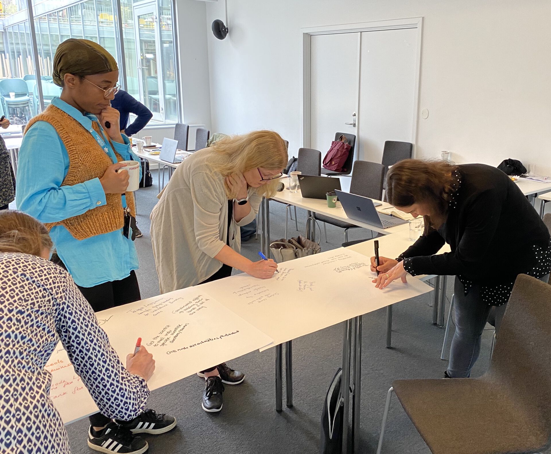Nordic EMBL meeting at NCMM in May 2022. Picture of 3 people writing on a large piece of paper on a table (group work)