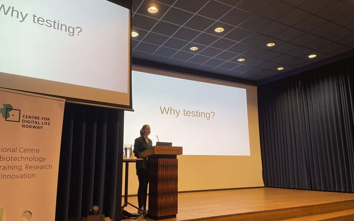 Presenter standing behind a lectern on a podium with a presentation slide entitled "Why testing".
