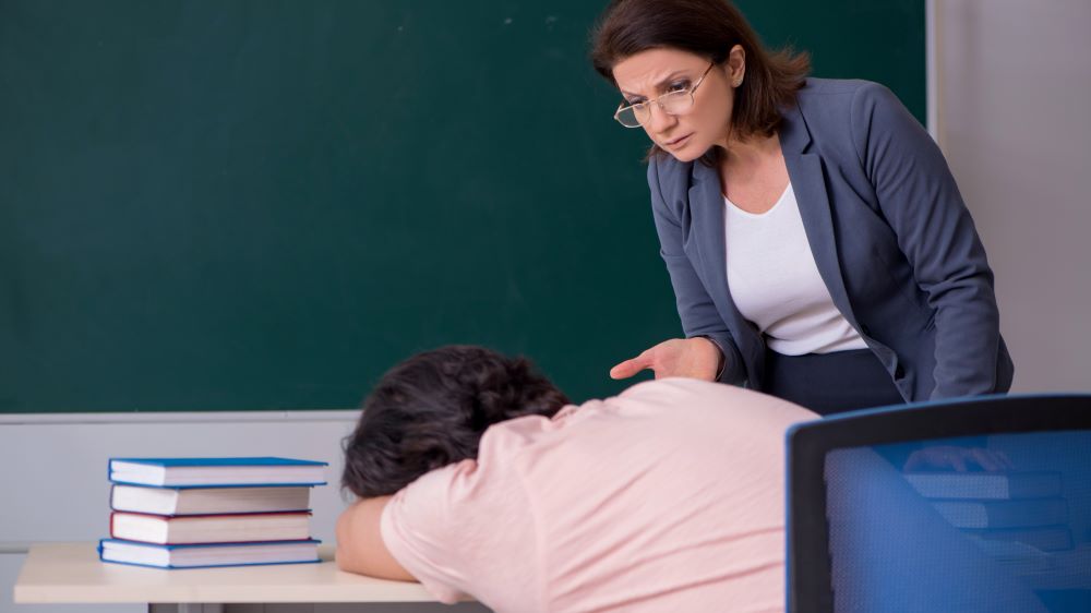 Oppgitt lærer ser på elev som har sovnet over pulten