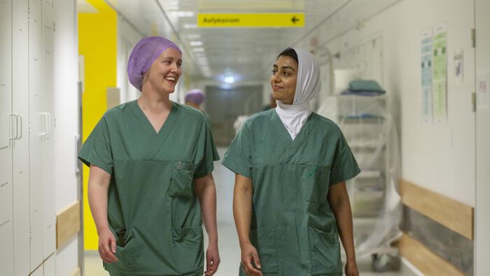 Bildet viser to studenter i sykehusuniform som g?r nedover en korridor