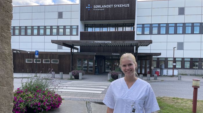 Bildet viser en kvinne i hvit uniform som står foran et sykehusbygg