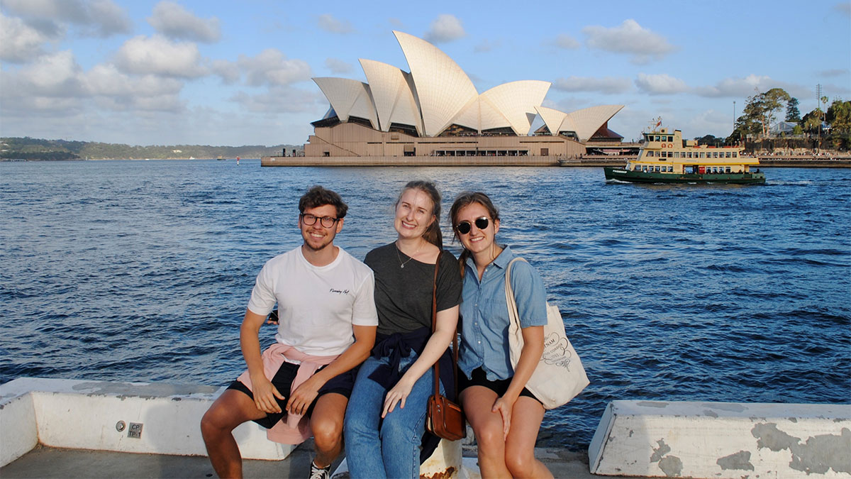 Tre studenter som sitter på bygga foran operahuset i Sydney.