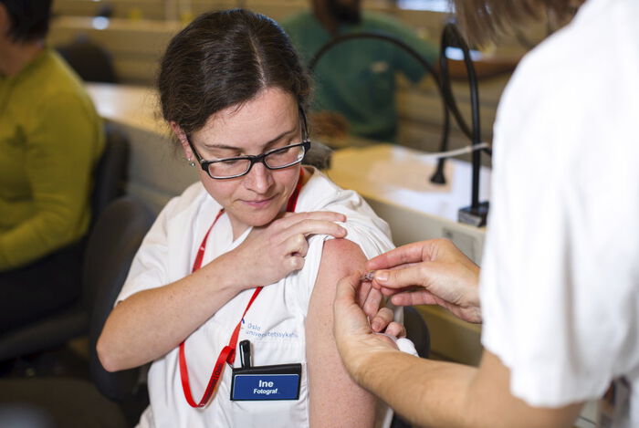 A woman in glasses and white clothing receives a vaccination.