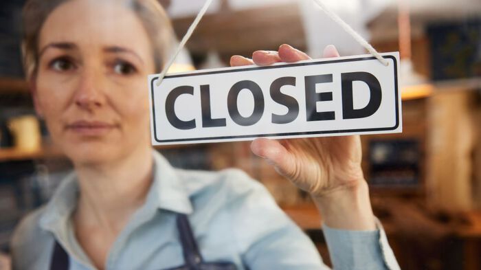 a woman holds a closed sign in a shop window